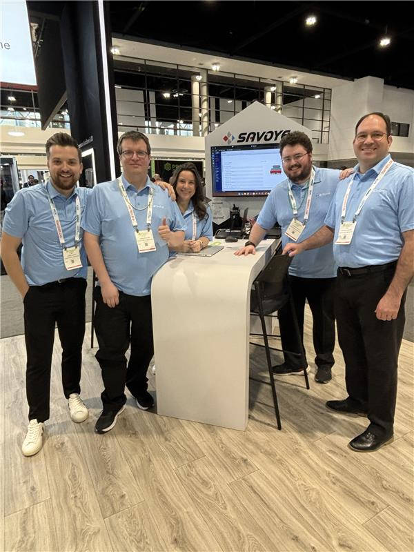 SAVOYE North America sales and engineering team at SAVOYE trade show exhibit SAVOYE North America sales and engineering team posing at the SAVOYE branded exhibit booth during an industry trade show, showcasing warehouse automation solutions