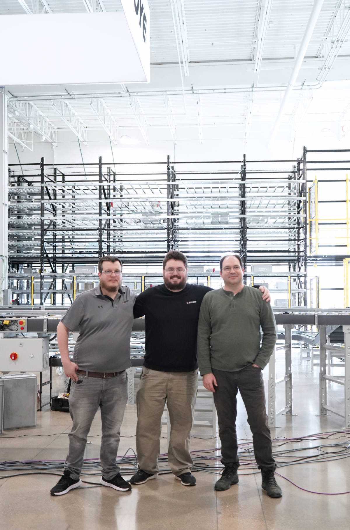 Three SAVOYE North America team members standing in front of automated shuttle storage racking system at the Aurora, Illinois headquarters and production center